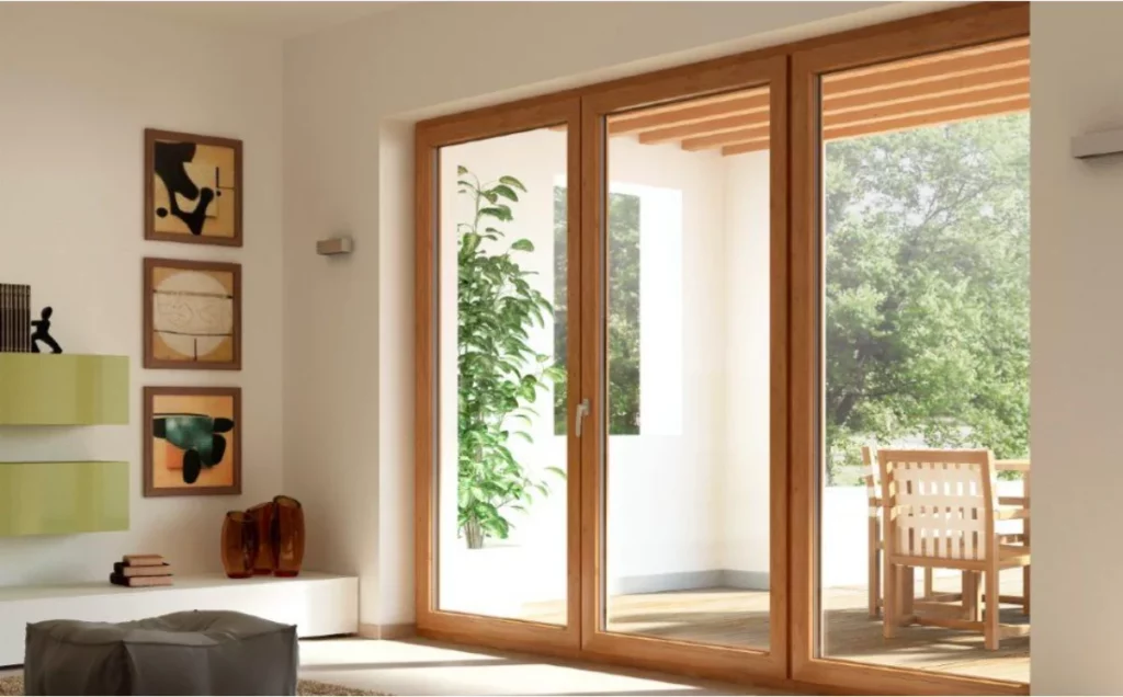 Porta-finestra scorrevole in legno naturale con triplo pannello che si affaccia su un patio con verde.