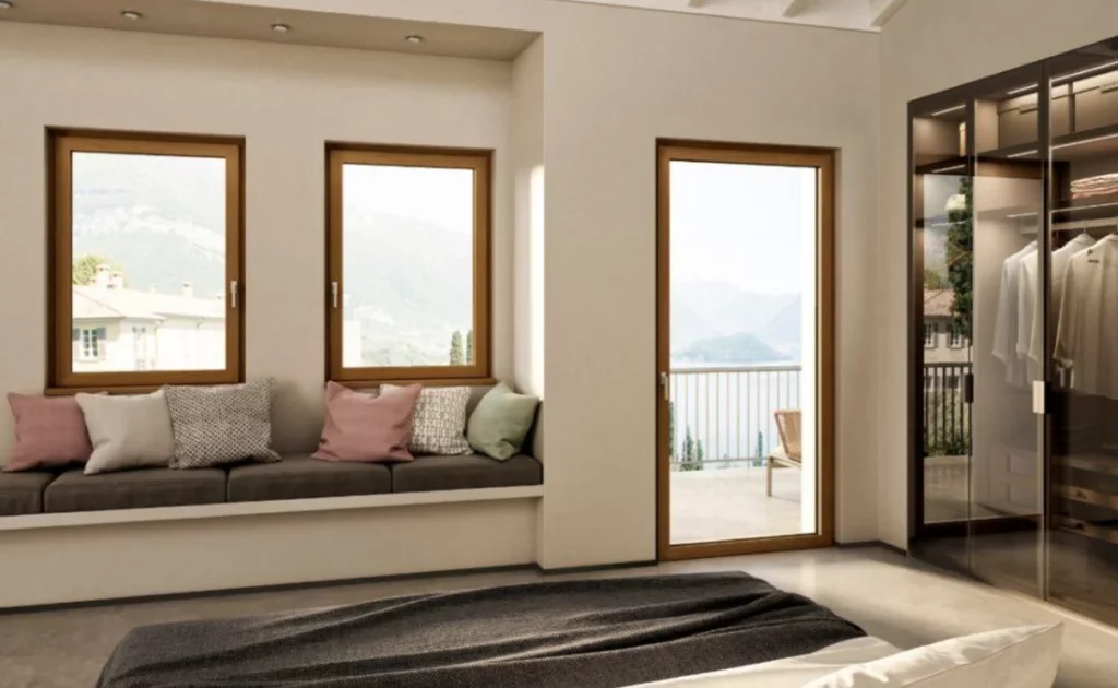 Camera da letto moderna con tre finestre e una porta-finestra in legno affacciate su un paesaggio montano e lago.