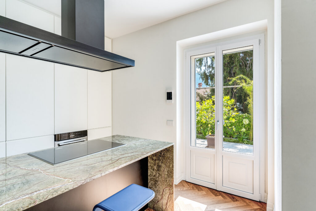 Portafinestra in PVC Oknoplast bianca con pannello bugnato installata in cucina moderna con vista su giardino esterno