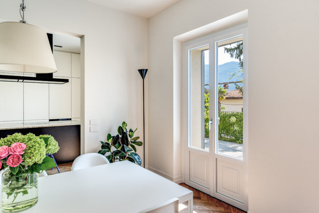Porta-finestra Prolux Evolution bianca con pannello bugnato inserita  in una cucina moderna e luminosa con dettagli minimal e fiori freschi sul tavolo