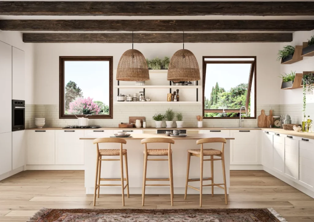 Cucina moderna luminosa con mobili bianchi, travi in legno, isola centrale e sgabelli in legno con seduta intrecciata.