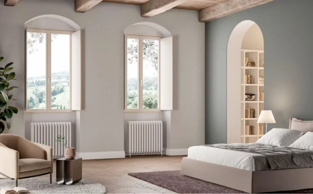Camera da letto rustica-chic con letto matrimoniale, poltrona, e finestre ad arco con vista paesaggio verde.