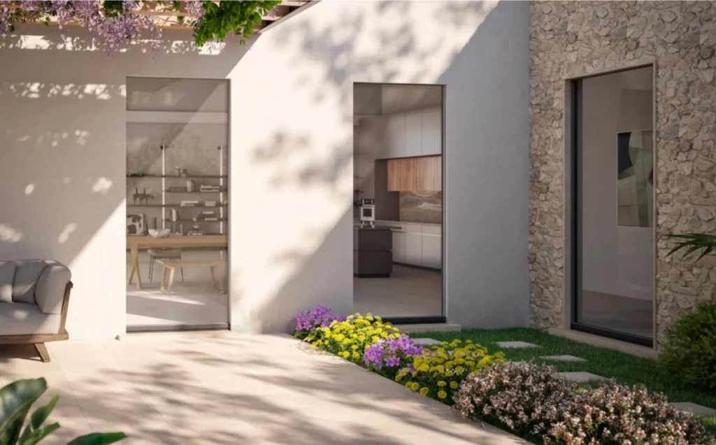 Cortile esterno con pavimento in pietra, aiuole fiorite viola e gialle, accesso a interni moderni.