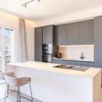 La cucina in laccato grigio è arricchita da un'elegante e pratica isola che mette in comunicazione la zona pranzo e il salotto con finestre Prolux Evolution di Oknoplast