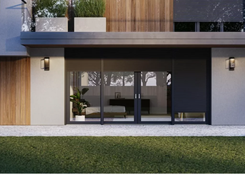 Finestra e portafinestra con tapparelle grigio scuro in una casa moderna. Piante sul balcone e lampade esterne su parete chiara. Giardino in primo piano.