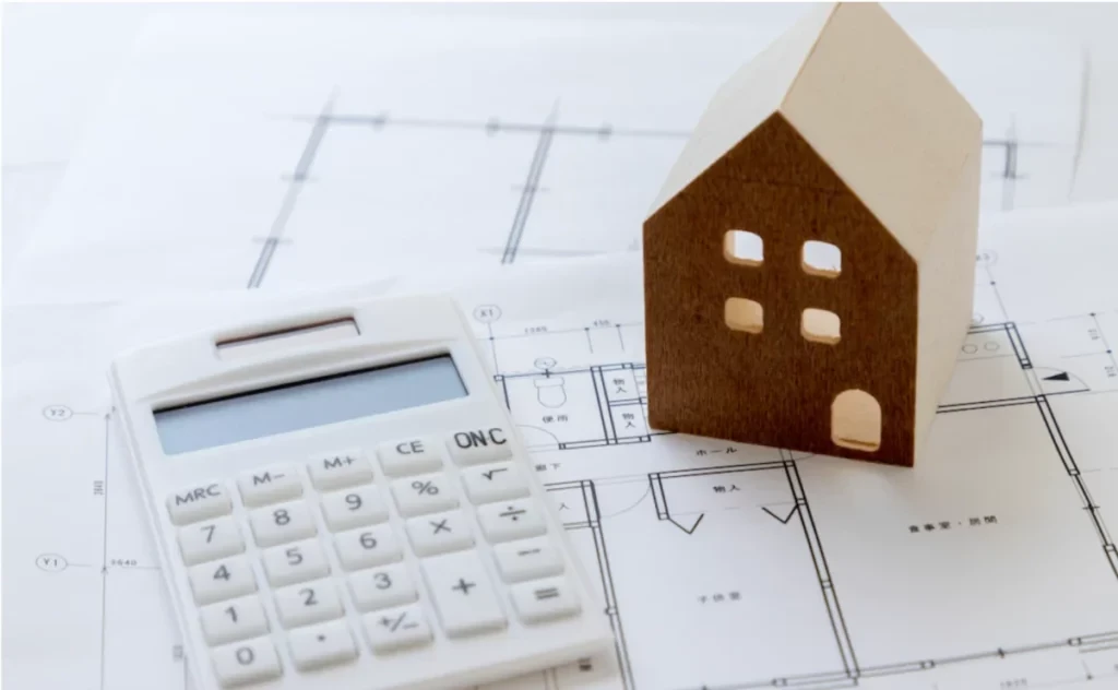 Calcolatrice, modellino di casa in legno e progetti architettonici per stime immobiliari