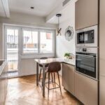 La cucina dai toni caldi presenta una pratica penisola con sgabelli davanti alle ampie finestre Prolux Evolution di Oknoplast